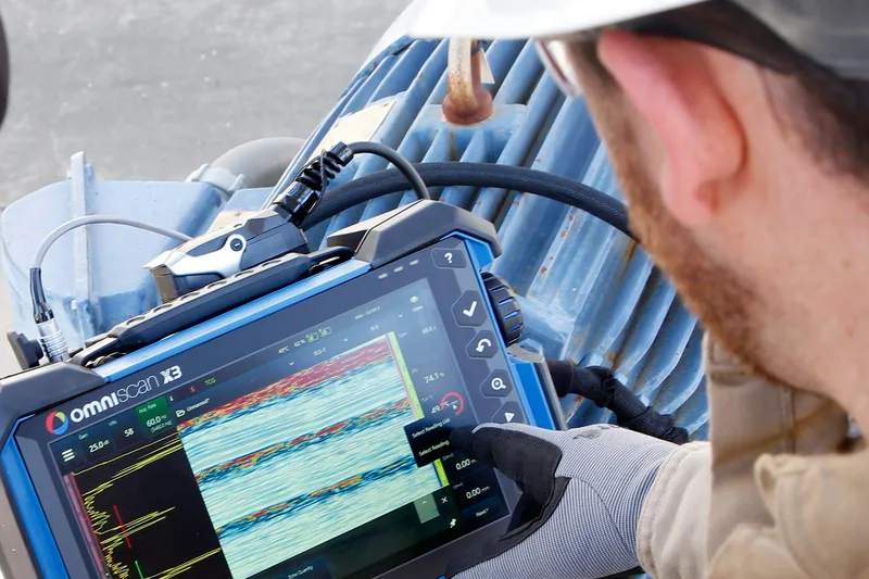 A technician in a hard hat reviewing ultrasonic test data on a flaw detector screen.